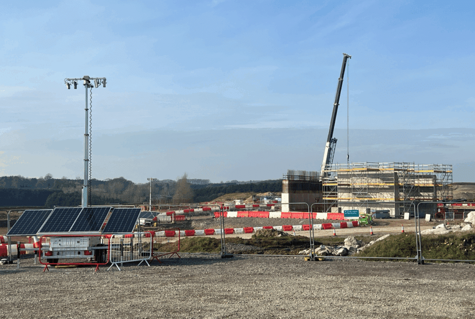 Construction site featuring a Prolectric ProLight mobile solar lighting tower with photovoltaic panels, a large crane, and scaffolding over a concrete structure.
